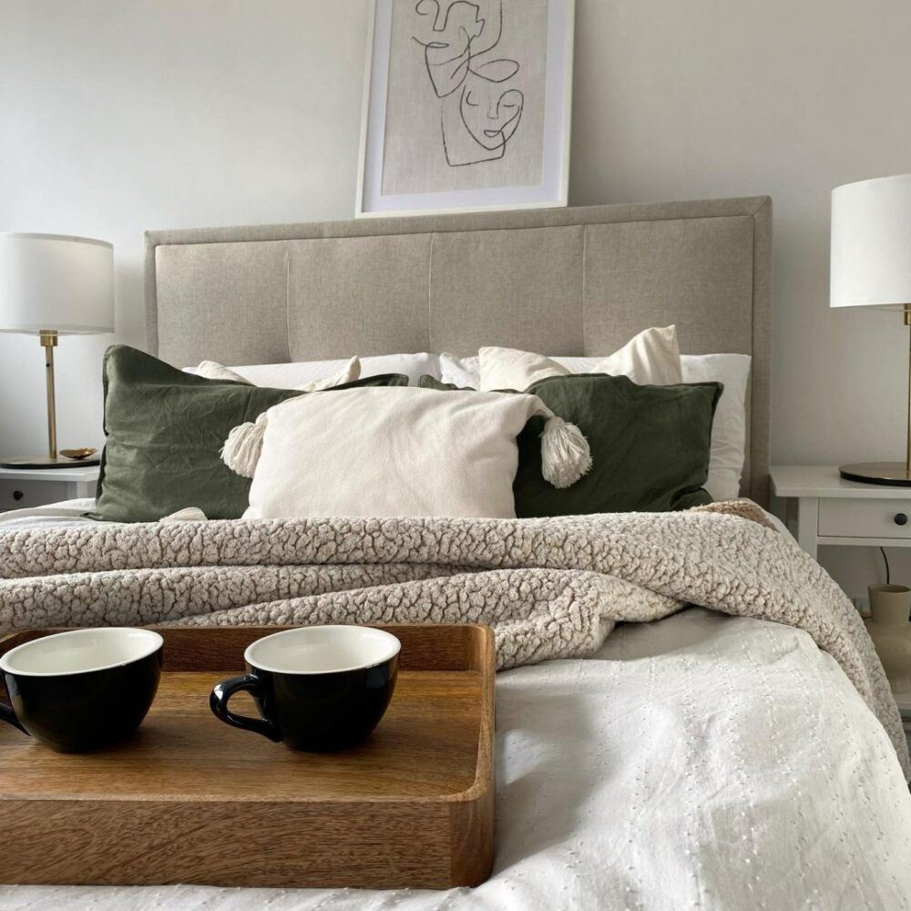 A natural upholstered bed frame, styled in a neutral white bedroom